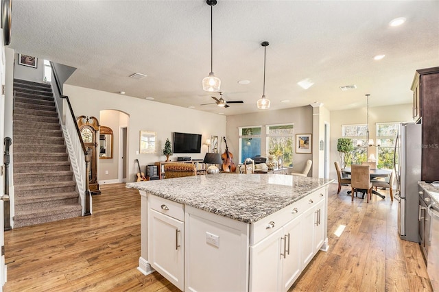 kitchen with arched walkways, light wood-style flooring, a center island, freestanding refrigerator, and light stone countertops