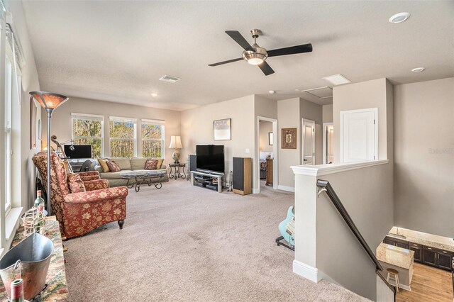 living area featuring a ceiling fan, visible vents, light carpet, and baseboards