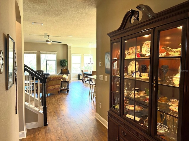 hall featuring a textured ceiling, visible vents, baseboards, stairway, and dark wood-style floors