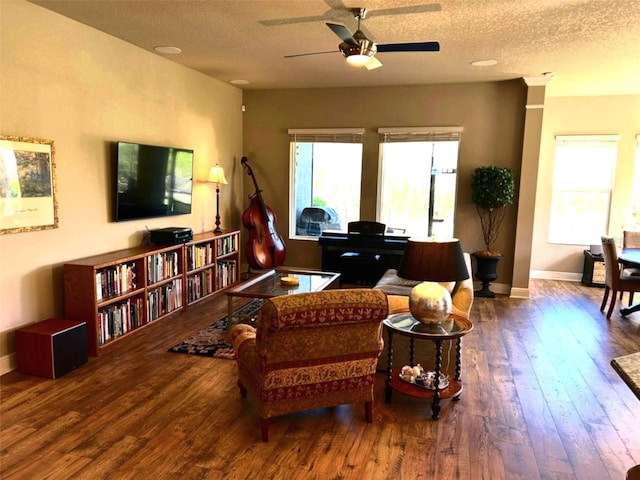 living room featuring a ceiling fan, a textured ceiling, baseboards, and wood finished floors