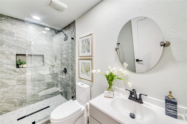 bathroom with vanity, toilet, and a tile shower