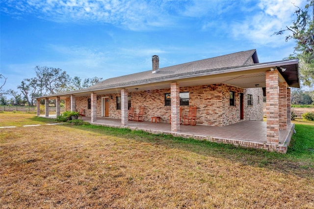 back of house featuring a patio area, a chimney, a lawn, and brick siding