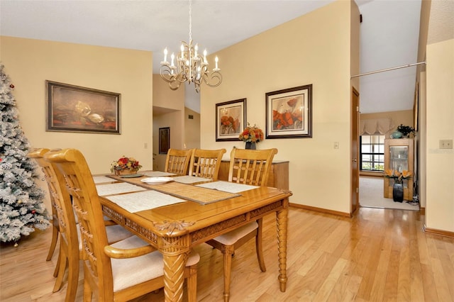 dining space with light wood-type flooring, an inviting chandelier, and lofted ceiling