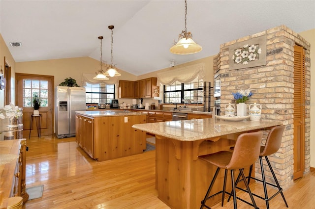 kitchen with stainless steel appliances, vaulted ceiling, light stone counters, and light wood finished floors