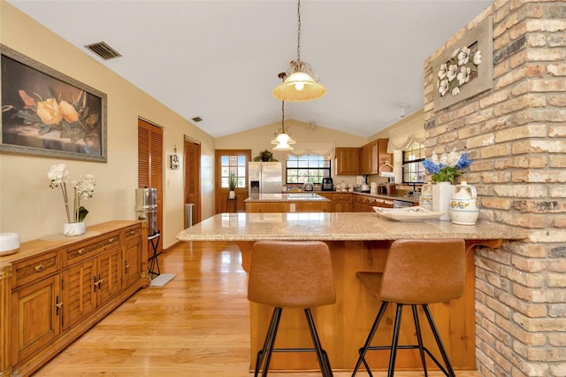 kitchen with stainless steel refrigerator with ice dispenser, brown cabinetry, light wood-style floors, vaulted ceiling, and a peninsula