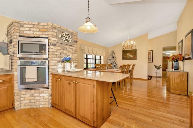 kitchen with stainless steel appliances, light stone counters, light hardwood / wood-style flooring, vaulted ceiling, and a kitchen bar