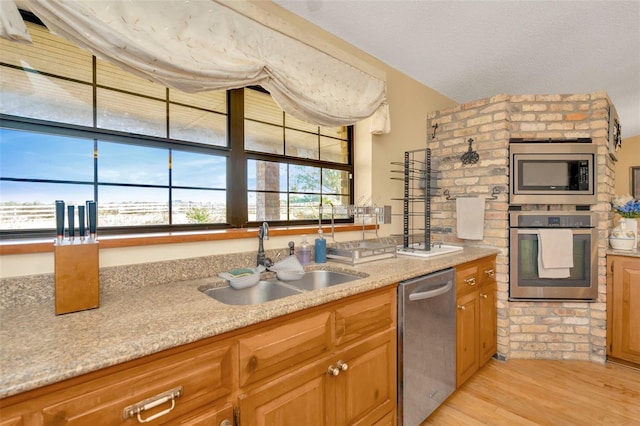 kitchen with brown cabinets, light countertops, appliances with stainless steel finishes, light wood-style floors, and a sink