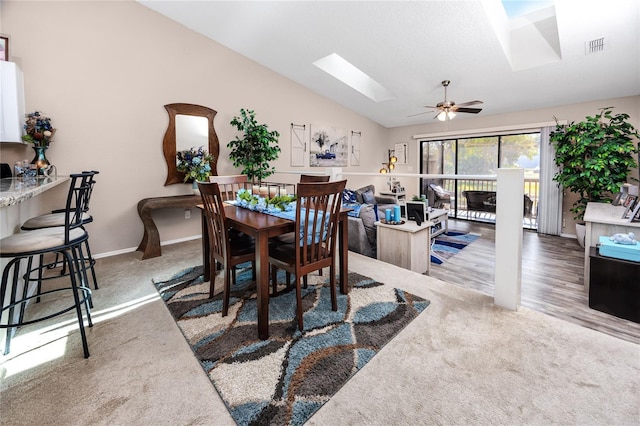 carpeted dining space featuring baseboards, visible vents, a ceiling fan, and vaulted ceiling with skylight