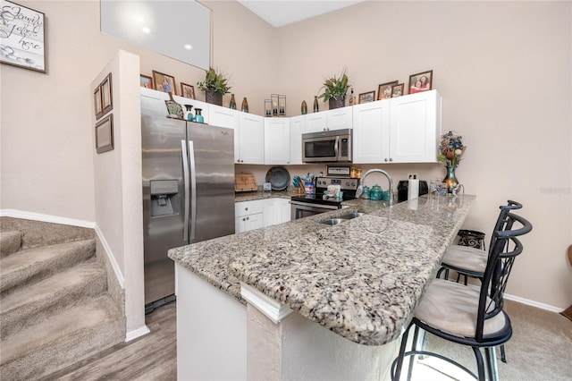 kitchen with a kitchen breakfast bar, light stone counters, a peninsula, white cabinets, and appliances with stainless steel finishes