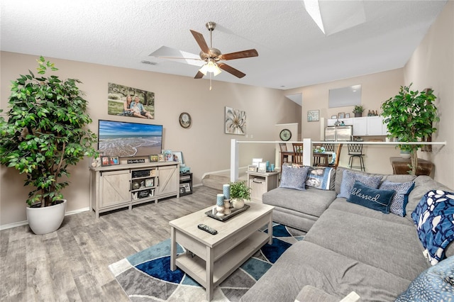 living area with baseboards, visible vents, a ceiling fan, and light wood finished floors