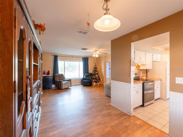 interior space with electric range, light wood-type flooring, white cabinetry, and hanging light fixtures