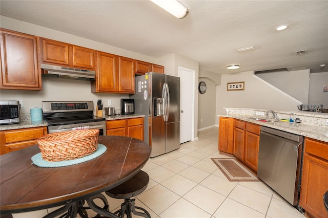 kitchen with light stone countertops, sink, stainless steel appliances, a textured ceiling, and light tile patterned floors