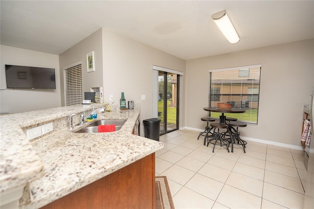 kitchen featuring light tile patterned flooring, light stone counters, and sink