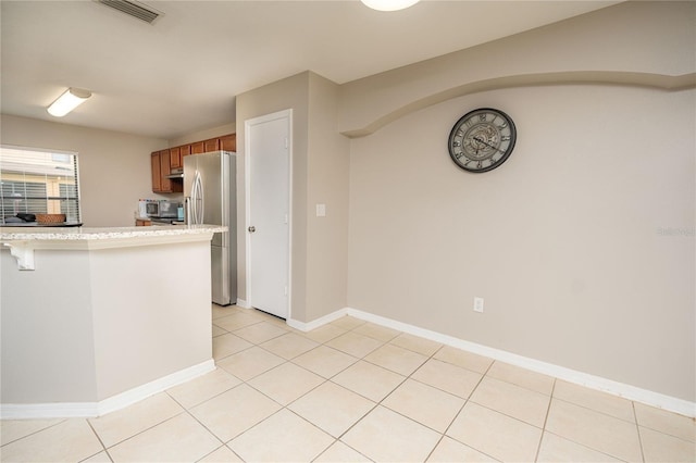 kitchen with a kitchen breakfast bar, kitchen peninsula, stainless steel fridge, and light tile patterned flooring