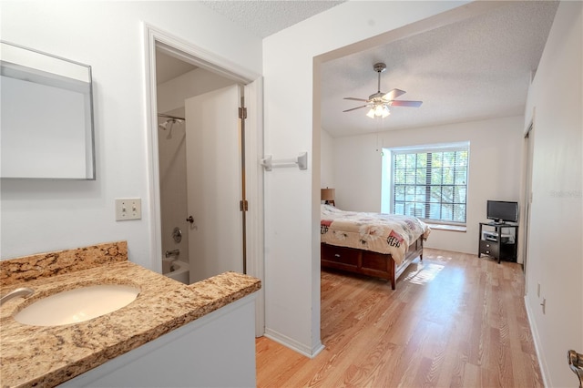 bedroom featuring sink, ceiling fan, a spacious closet, a textured ceiling, and light hardwood / wood-style floors