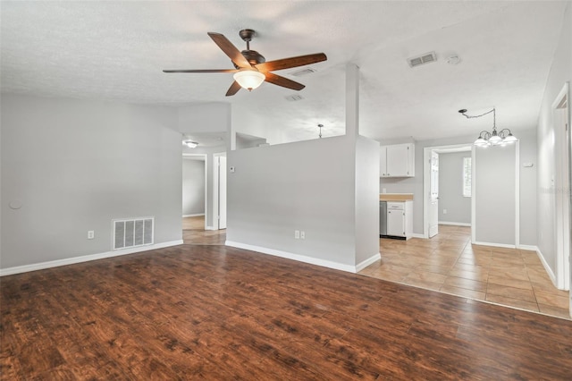 unfurnished living room with lofted ceiling, ceiling fan with notable chandelier, light hardwood / wood-style floors, and a textured ceiling