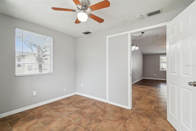 tiled spare room featuring a textured ceiling, ceiling fan, and a healthy amount of sunlight