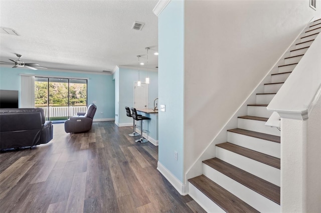 staircase featuring ceiling fan, ornamental molding, wood-type flooring, and a textured ceiling