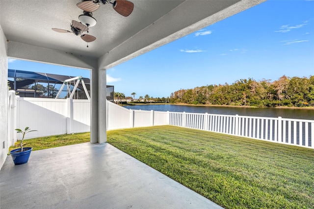 view of yard featuring ceiling fan, a patio, glass enclosure, and a water view