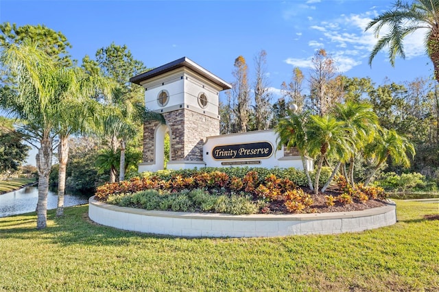 community / neighborhood sign featuring a water view and a lawn