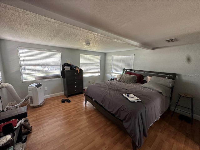 bedroom with hardwood / wood-style flooring, beam ceiling, and a textured ceiling