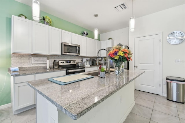 kitchen with white cabinetry, backsplash, decorative light fixtures, a center island with sink, and appliances with stainless steel finishes