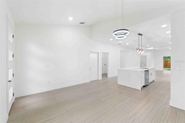 kitchen featuring stainless steel dishwasher, a kitchen island with sink, sink, white cabinetry, and hanging light fixtures