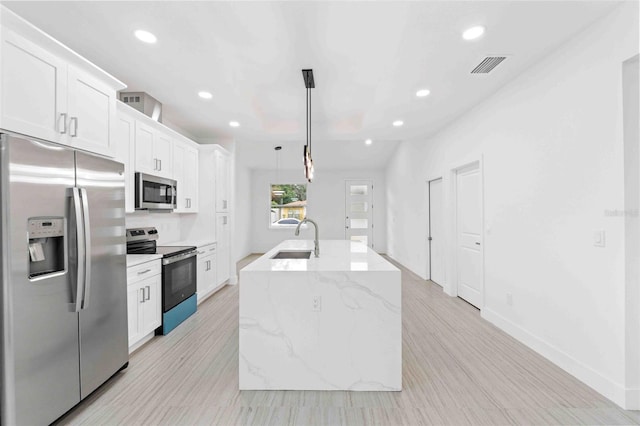 kitchen with a center island with sink, white cabinets, hanging light fixtures, and appliances with stainless steel finishes