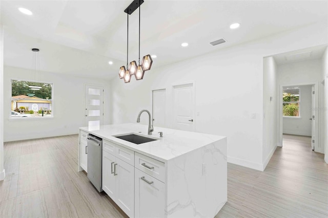 kitchen with pendant lighting, white cabinets, light stone countertops, an island with sink, and light hardwood / wood-style floors