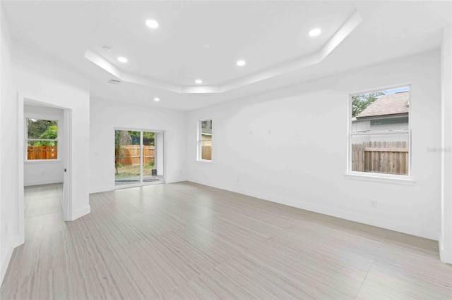 unfurnished room with a raised ceiling, plenty of natural light, and light hardwood / wood-style floors