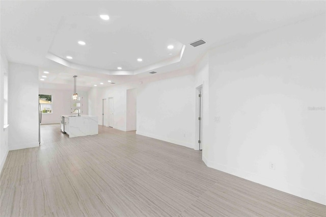 empty room with a tray ceiling, sink, and light hardwood / wood-style floors