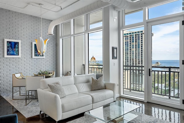 living room with expansive windows, a water view, a high ceiling, and brick wall