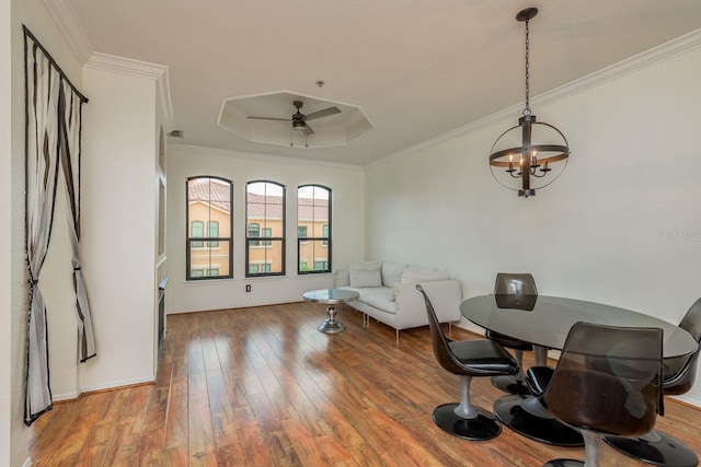 dining space with a raised ceiling, hardwood / wood-style floors, ceiling fan with notable chandelier, and ornamental molding