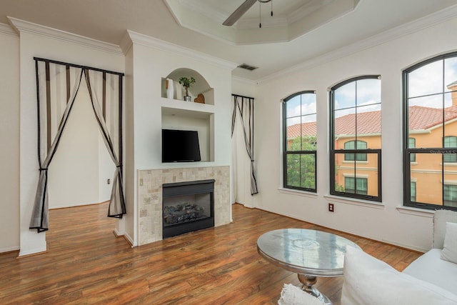 living room featuring hardwood / wood-style floors, ceiling fan, ornamental molding, and a tile fireplace