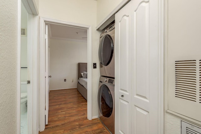 laundry room featuring dark hardwood / wood-style flooring, ornamental molding, and stacked washer and clothes dryer