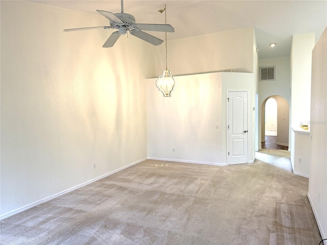 empty room with light carpet, visible vents, arched walkways, baseboards, and a high ceiling