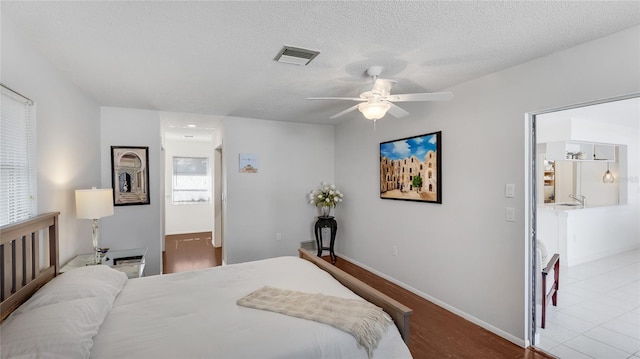 bedroom with ensuite bath, light hardwood / wood-style flooring, ceiling fan, multiple windows, and a textured ceiling