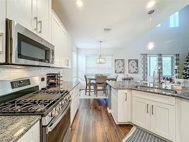 kitchen with pendant lighting, appliances with stainless steel finishes, white cabinets, dark hardwood / wood-style flooring, and dark stone counters