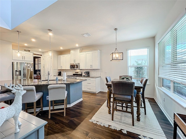 kitchen featuring appliances with stainless steel finishes, a kitchen island with sink, pendant lighting, and white cabinets