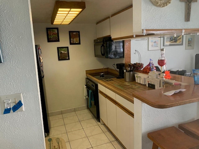 kitchen with light tile patterned flooring, white cabinets, and black appliances