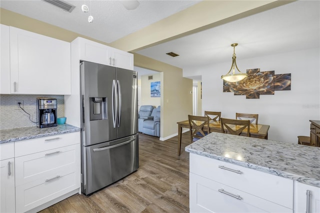 kitchen with backsplash, white cabinets, light wood-type flooring, decorative light fixtures, and stainless steel fridge with ice dispenser