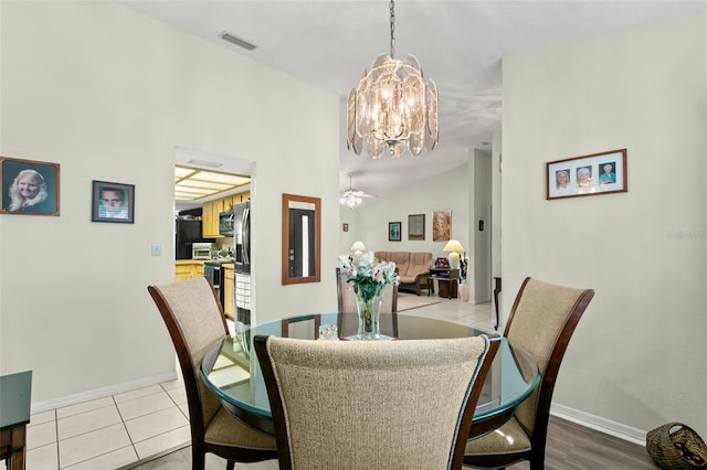 tiled dining space featuring ceiling fan with notable chandelier and vaulted ceiling