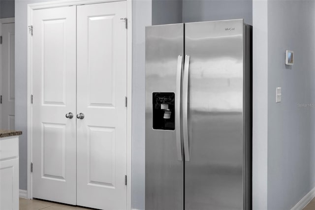 kitchen with dark stone countertops, stainless steel fridge with ice dispenser, white cabinets, and light tile patterned floors