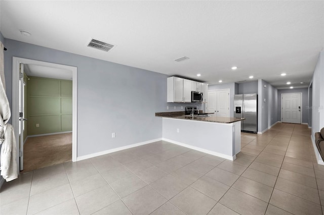 kitchen with sink, light tile patterned floors, kitchen peninsula, white cabinets, and appliances with stainless steel finishes