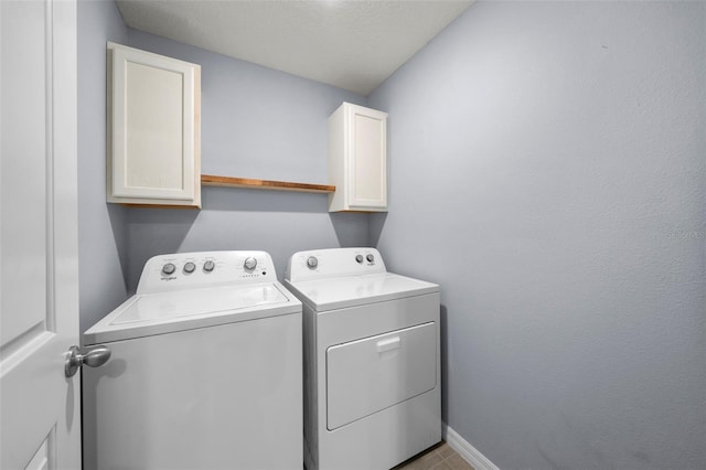 laundry area with washer and dryer, a textured ceiling, and cabinets