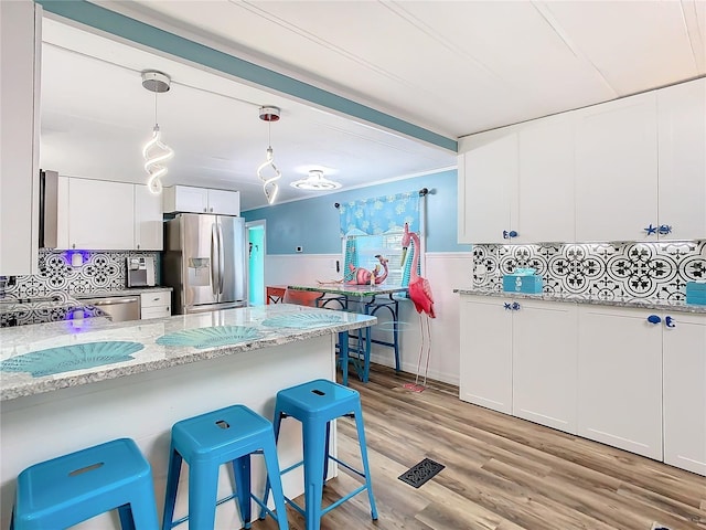 kitchen with appliances with stainless steel finishes, a kitchen breakfast bar, pendant lighting, light hardwood / wood-style flooring, and white cabinetry