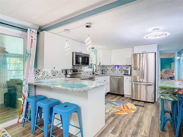 kitchen featuring pendant lighting, backsplash, white cabinets, light hardwood / wood-style flooring, and stainless steel appliances