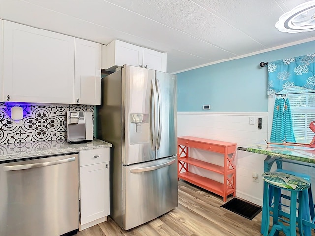 kitchen with light stone countertops, appliances with stainless steel finishes, ornamental molding, white cabinets, and light hardwood / wood-style floors