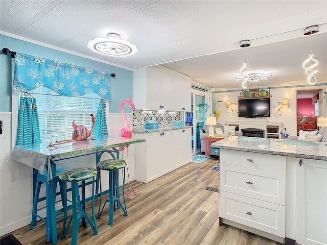 kitchen with white cabinets, light stone counters, light wood-type flooring, and ornamental molding