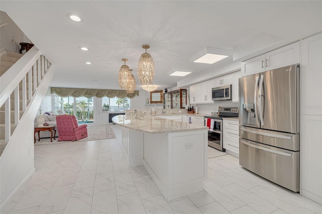 kitchen with pendant lighting, white cabinets, a kitchen island, light stone counters, and stainless steel appliances